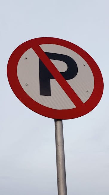 A round 'No Parking' sign featuring a black letter 'P' with a red diagonal line crossing it, mounted on a silver metal pole against a cloudy grey sky. The sign is situated outdoors, likely near a property involved in home relocation or furniture transport activities. The background shows an overcast sky, providing natural diffused lighting. This signage is important to consider for vehicle positioning and loading during house removals, as managed by Man and Van Kennington, who specialise in packing and moving services in the Lambeth area.